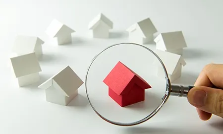 White houses and 1 red house and hand handling the magnifying glass